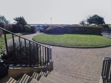 A paved pathway leading to a grassy garden with bushes and trees surrounded by a black metal fence at Ismay Dining Room Suite - Titanic Interest in Waterloo Merseyside
