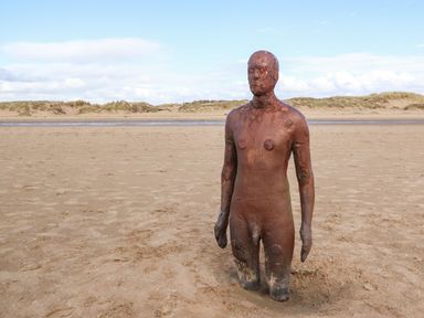 A beach with a rusted metal sculpture of a human figure partially buried in sand at Ismay Dining Room Suite - Titanic Interest in Waterloo Merseyside