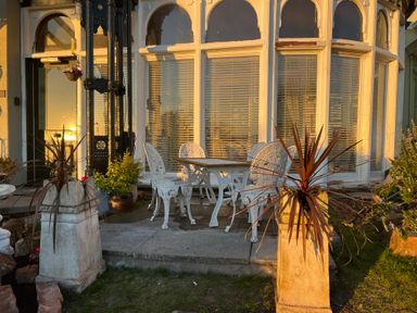 An outdoor patio with a white metal table and six chairs in front of large windows with blinds at Ismay Dining Room Suite - Titanic Interest in Waterloo Merseyside