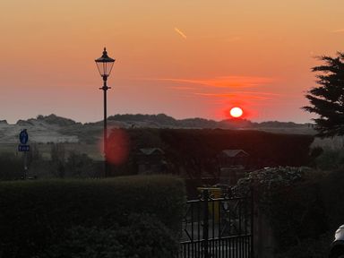 Sunset over a landscape with a lamppost bushes a gate and wind turbines in the distance at Ismay Dining Room Suite - Titanic Interest in Waterloo Merseyside