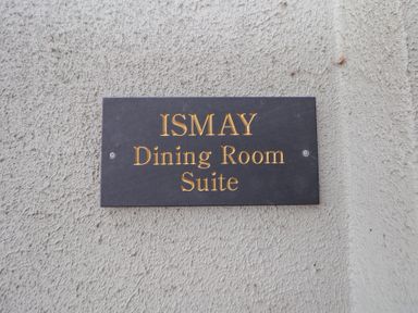 A black rectangular plaque with gold lettering reading Ismay Dining Room Suite mounted on a textured light-colored wall at Ismay Dining Room Suite - Titanic Interest in Waterloo Merseyside