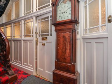 A hallway with a wooden grandfather clock near a white door and panelled walls with textured glass windows at Ismay Dining Room Suite - Titanic Interest in Waterloo Merseyside