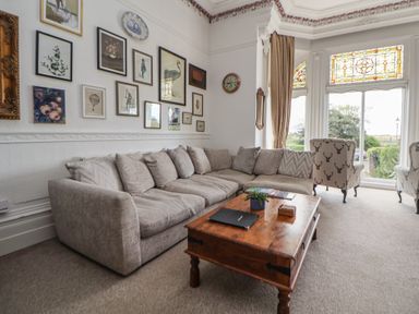 A sitting room with a large corner sofa a wooden coffee table and decorative wall art at Ismay Dining Room Suite - Titanic Interest in Waterloo Merseyside