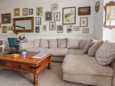 A living room with a beige sectional sofa wooden coffee table and framed pictures on the wall at Ismay Dining Room Suite - Titanic Interest Waterloo Merseyside