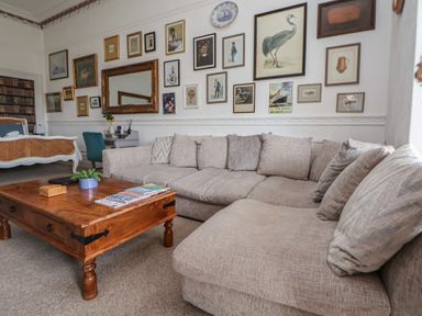 A living room with a beige sectional sofa a wooden coffee table and framed pictures on the wall at Ismay Dining Room Suite - Titanic Interest Waterloo Merseyside