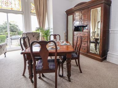 A dining room with wooden table and chairs near large windows and a wooden cabinet with mirrors at Ismay Dining Room Suite - Titanic Interest in Waterloo Merseyside