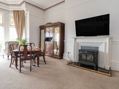 A dining room with a wooden table and chairs next to an armchair and a cabinet a fireplace with a television above at Ismay Dining Room Suite - Titanic Interest in Waterloo Merseyside
