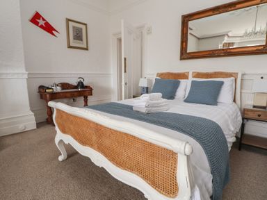 A bedroom with a double bed with blue pillows and blanket a wooden table with a kettle and cups and a large mirror on the wall at Ismay Dining Room Suite - Titanic Interest in Waterloo Merseyside