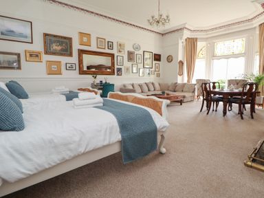 A large room with two beds a sofa a coffee table a dining table with chairs and framed pictures on the walls at Ismay Dining Room Suite - Titanic Interest in Waterloo Merseyside