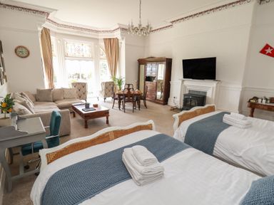 A bedroom with two single beds with blue throws a sofa a coffee table a dining table a wardrobe and a television at Ismay Dining Room Suite - Titanic Interest Waterloo Merseyside