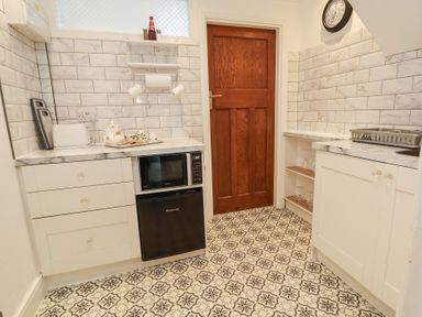 A kitchen with white cabinets a microwave a small fridge a wooden door and patterned floor tiles at Ismay Dining Room Suite - Titanic Interest in Waterloo Merseyside