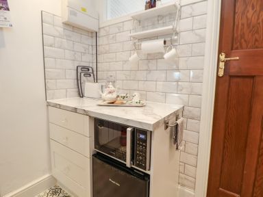A small kitchen corner with a countertop holding a teapot set and cookies a microwave and a mini fridge below with a wooden door to the side Ismay Dining Room Suite - Titanic Interest Waterloo Merseyside