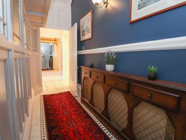 A hallway with a red runner rug a wooden sideboard with plants blue walls and framed pictures at Ismay Dining Room Suite - Titanic Interest in Waterloo Merseyside