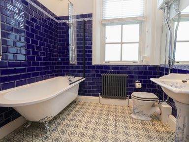 A bathroom with a clawfoot bathtub toilet sink patterned floor tiles and blue tiled walls at Ismay Dining Room Suite Titanic Interest Waterloo Merseyside