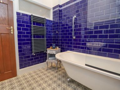 A bathroom with blue tiled walls a white bathtub a wooden door a radiator and a small table with toiletries at Ismay Dining Room Suite - Titanic Interest Waterloo Merseyside