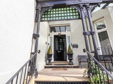 Front entrance with black door flanked by two potted plants and a bench on the right at Ismay Dining Room Suite - Titanic Interest in Waterloo Merseyside