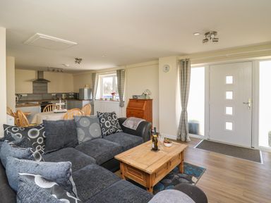 A living room with a dark sofa and wooden coffee table next to a front door and an open kitchen with a dining table at Brynteg Cottage in Tegryn