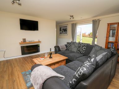 A living room with a black sectional sofa a wooden coffee table and a wall-mounted television at Brynteg Cottage in Tegryn