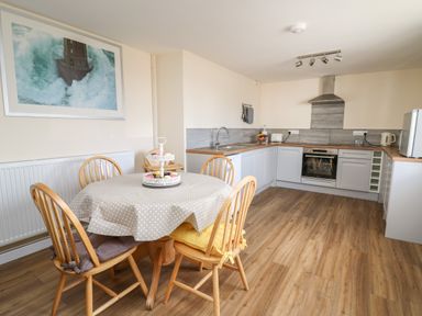 A kitchen with wooden table and chairs a tablecloth and a framed picture on the wall at Brynteg Cottage in Tegryn