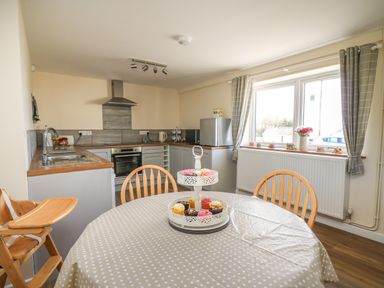 A kitchen with wooden chairs around a polka dot covered table and cupcakes on a stand at Brynteg Cottage in Tegryn
