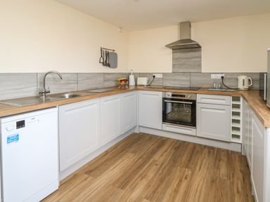 A kitchen with white cabinets wooden countertops an oven stovetop sink dishwasher and various kitchen utensils at Brynteg Cottage in Tegryn