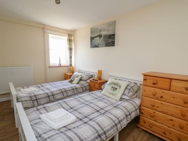 A bedroom with two single beds beside bedside tables and a wooden dresser at Brynteg Cottage in Tegryn