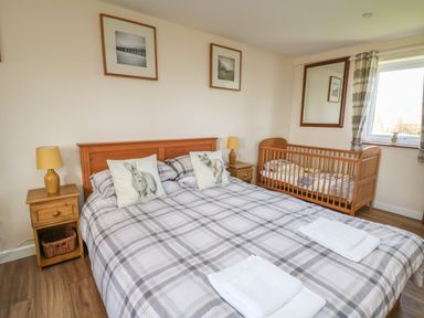 A bedroom with a double bed and a wooden crib near a window at Brynteg Cottage in Tegryn