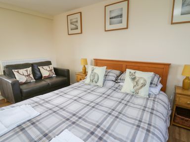 A bedroom with a double bed with animal print cushions a black sofa with deer cushions and wooden bedside tables at Brynteg Cottage in Tegryn