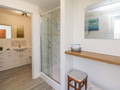 A bathroom with a glass shower enclosure a wooden stool a wooden shelf with toiletries a large mirror and a sink with cabinets at Brynteg Cottage in Tegryn