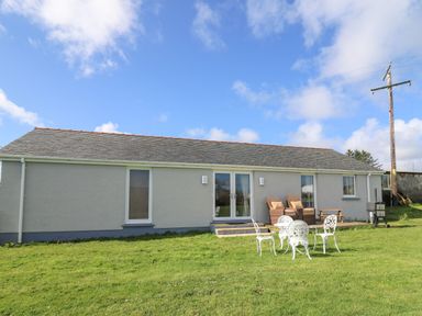 A single-story building with patio doors and outdoor chairs on a grassy lawn at Brynteg Cottage in Tegryn