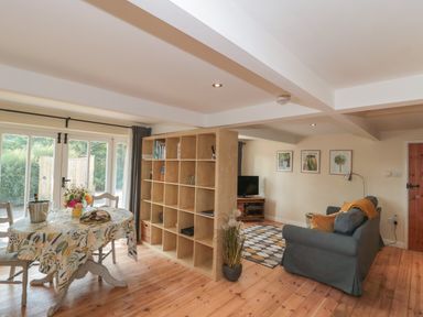 A living and dining area with a table and chairs beside a large shelving unit and a sofa with a television on a stand at Nuthatch in Honiton