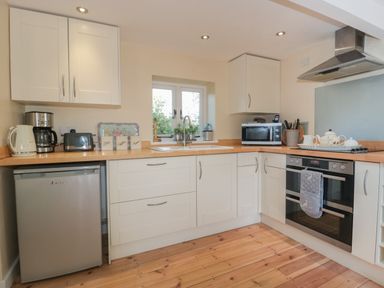 A kitchen with white cabinets wooden countertops appliances and a window at Nuthatch Honiton