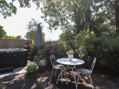 An outdoor seating area with a round table and two chairs next to a hot tub and surrounded by plants at Nuthatch in Honiton