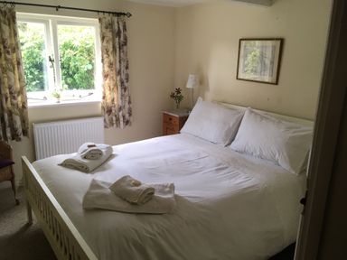 A bedroom with a double bed with white bedding and towels on top next to a window with floral curtains at Nuthatch in Honiton