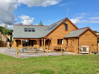 A wooden house with a slate roof and outdoor seating area surrounded by a wooden fence at Riverside Lodge in Washford