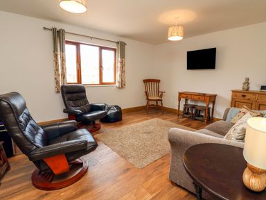 A living room with two black leather chairs a sofa a wooden table with lamp a wall mounted TV and wooden furniture at Riverside Lodge in Washford