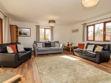 A living room with sofas cushions wooden shelves and windows at Riverside Lodge in Washford