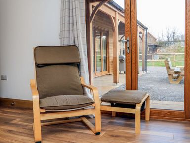 A chair with an ottoman in front of a glass door showing an outdoor wooden structure at Riverside Lodge in Washford