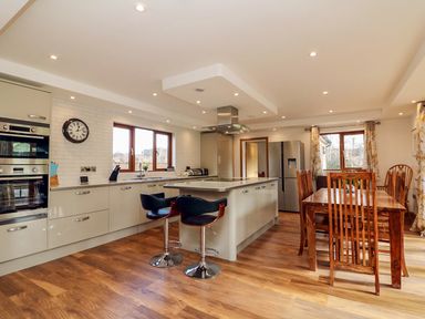 A kitchen with an island and two bar stools next to a wooden dining table with six chairs at Riverside Lodge in Washford