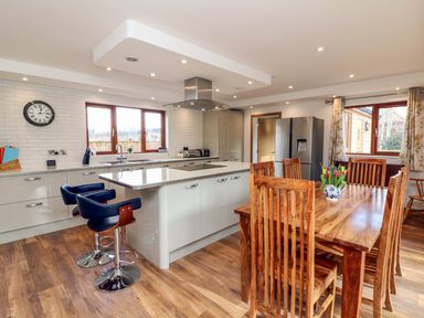 A kitchen with an island, bar stools, wooden dining table and chairs and a refrigerator at Riverside Lodge in Washford