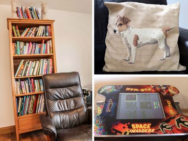 A wooden bookshelf filled with books next to a black leather chair a cushion with a dog embroidery on a black leather chair and a retro arcade game table with Space Invaders artwork
