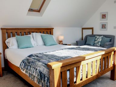 A bedroom with a wooden bed with blue pillows and a blanket and a grey sofa with cushions at Riverside Lodge in Washford