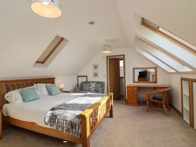 An attic bedroom with a wooden bed a sofa a desk with a chair and skylight windows at Riverside Lodge in Washford