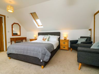 A bedroom with a double bed two bedside tables two armchairs a wooden dressing table and a skylight window at Riverside Lodge in Washford