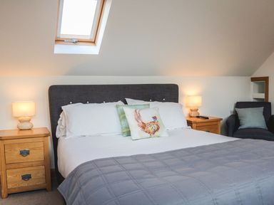 A bedroom with a bed gray headboard bedside tables lamps and a chair at Riverside Lodge in Washford