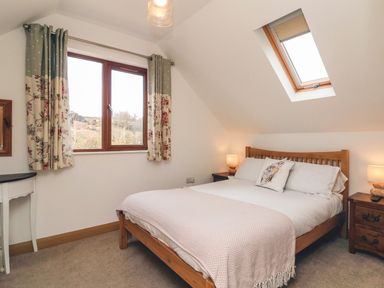 A bedroom with a wooden bed frame a skylight window and a window with curtains at Riverside Lodge in Washford