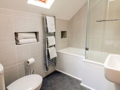 A bathroom with a toilet a towel rack with towels a bathtub with a glass shower screen and a sink at Riverside Lodge in Washford