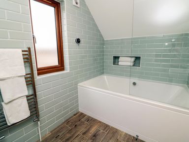 A bathroom with a bathtub a window with wooden frame a towel rack with towels and tiled walls at Riverside Lodge in Washford