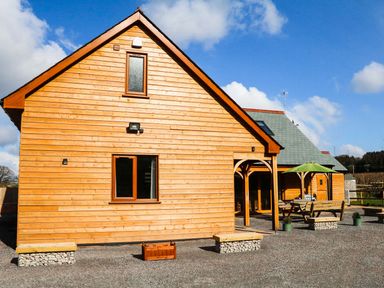An exterior view of a wooden house with a small covered porch and outdoor seating area at Riverside Lodge in Washford