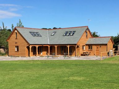 A wooden house with multiple skylights and outdoor seating on a green lawn at Riverside Lodge in Washford